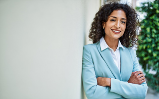 A woman in professional attire with her arms crossed and a confident smile